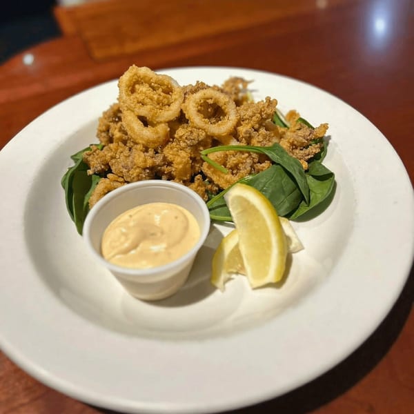 Crispy fried calamari rings and tentacles on a bed of spinach, with lemon wedges and dipping sauce.