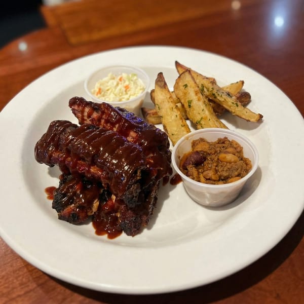 BBQ ribs with sauce, coleslaw, baked beans, and seasoned fries on a white plate.