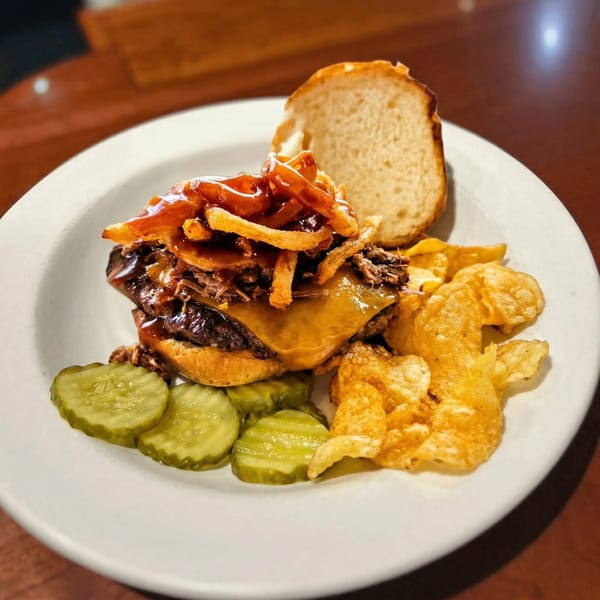 A BBQ burger with melted cheese, crispy onions, pickles, and potato chips on a white plate.