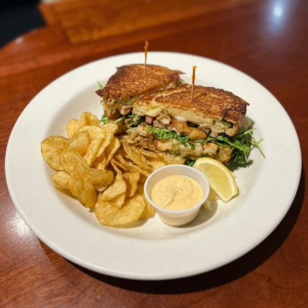 A grilled sandwich with chips, sauce, and a lemon wedge on a white plate.